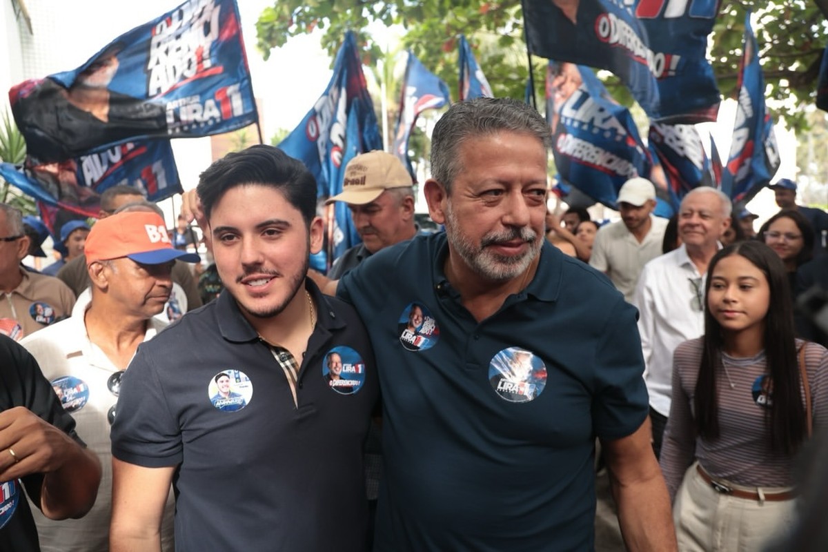 Alvinho Lira e seu pai, Arthur Lira, caminham juntos em meio a apoiadores durante evento de campanha eleitoral.