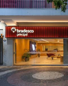 Fachada de agência Bradesco Principal com letreiro iluminado e interior moderno visível através de porta de vidro.