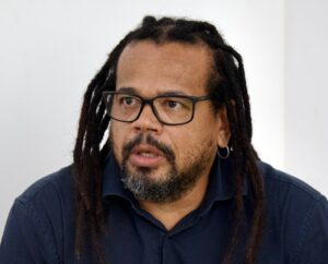 Kleber Rosa, homem negro de dreadlocks e óculos, veste camisa azul escura e fala durante entrevista.