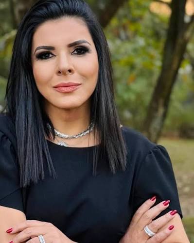 Mara Maravilha posa para foto com expressão séria, vestindo blusa preta e usando colares e anéis.