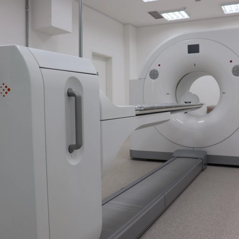 Equipamento de PET-CT branco instalado em sala clínica com piso claro e iluminação de teto.