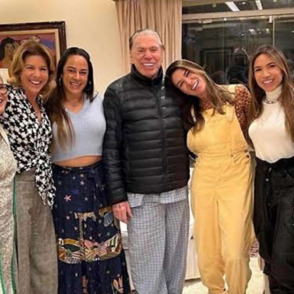 Silvio Santos sorridente posa abraçado com suas filhas em um encontro familiar.