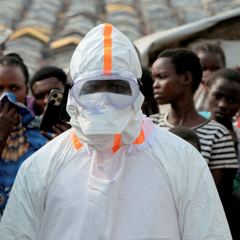Profissional de saúde com traje de proteção completo em meio a uma multidão na República Democrática do Congo.